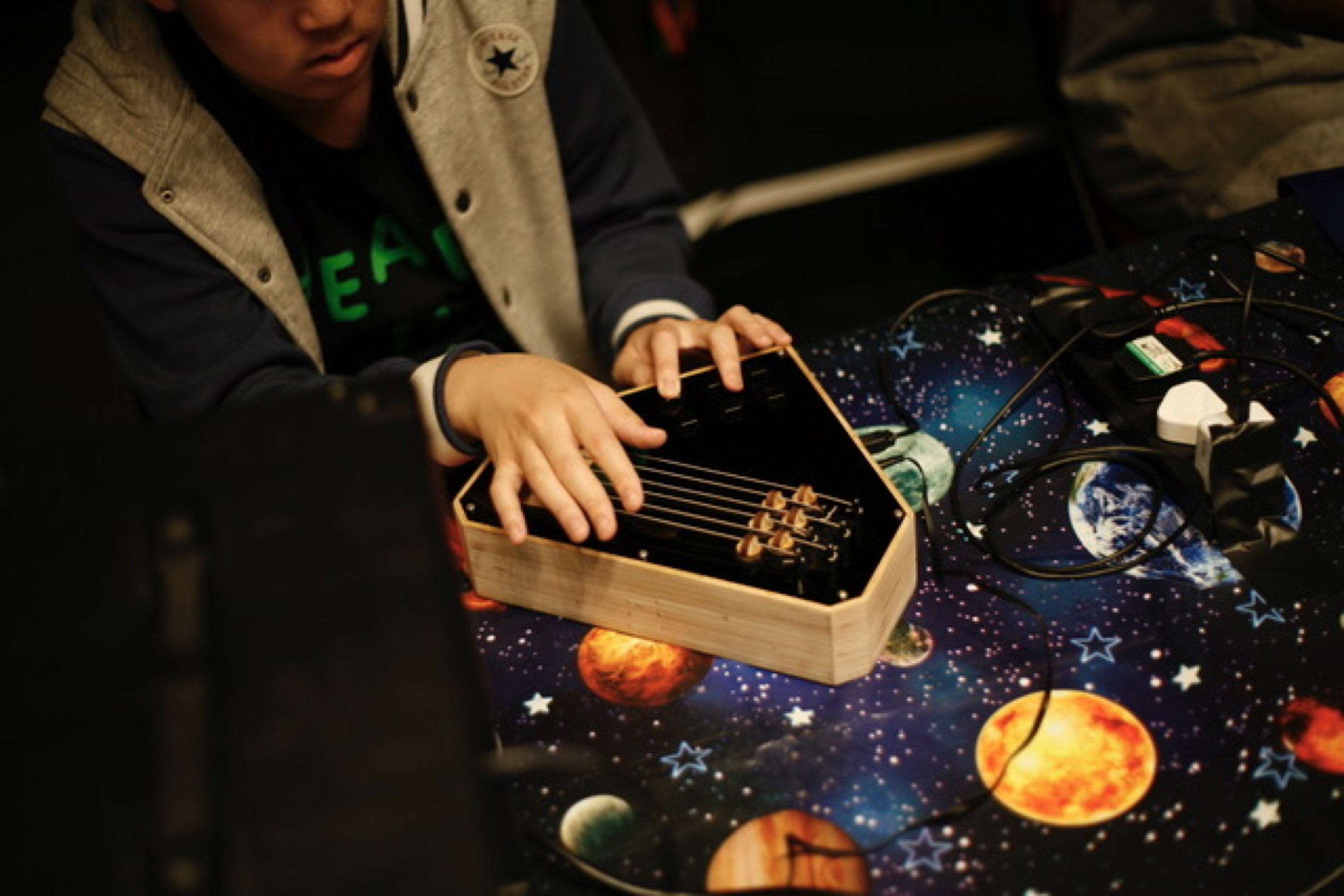 Peripersonal Modular Interfaces — a young musician playing a wooden, six-stringed hexagonal sensing tile placed on a starry-print fabric table during a community music workshop
